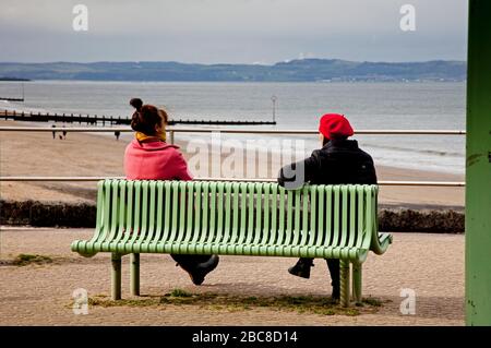 Portobello Beach, Édimbourg, Écosse, Royaume-Uni. 3 avril 2020. Nuageux à 8 degrés centigrade, deux femmes distanciation sociale sur un banc, il semble que la plupart du public prennent en compte l'avertissement du gouvernement au sujet de rester à la maison pour éviter le risque de capturer le Coronavirus Covid-19. Quelques personnes utilisant la promenade et la plage pour leurs exercices quotidiens autorisés et pour marcher leurs chiens. Edimbourg devrait s'attendre à une température de 16 degrés dimanche qui pourrait faire sortir la foule. Banque D'Images