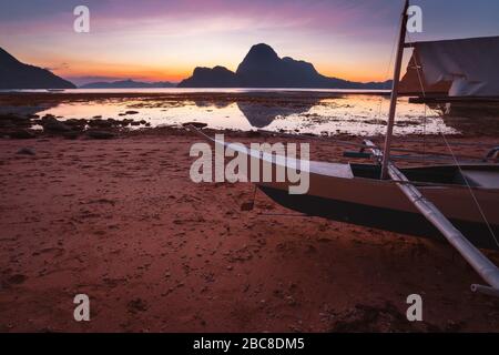 Baie El Nido avec bateau banca local sur la rive au coucher du soleil à marée basse. Paysage nature pittoresque. Palawan, Philippines. Banque D'Images