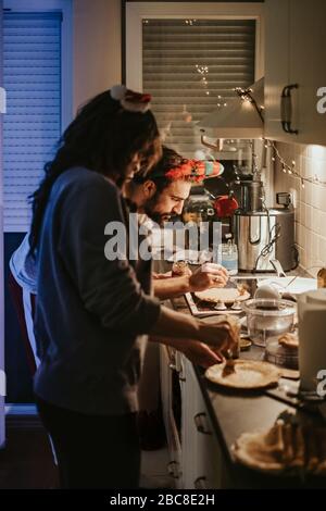 Homme sérieux avec femme à côté de lui répandant la crème sur la crêpe dans la cuisine à une nouvelle veille d'années Banque D'Images