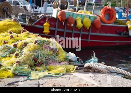 Des filets de pêche se sont accumulés sur le côté d'une marina de l'île grecque de Crète, avec un petit bateau de pêche rouge en arrière-plan Banque D'Images