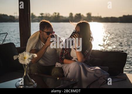 Couple boire du café au bord de la rivière au coucher du soleil. Magnifique journée d'automne Banque D'Images