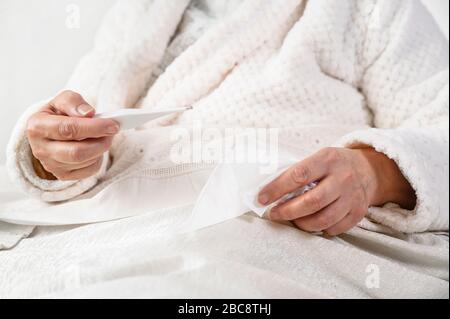 Coronavirus. Malade senior femme tenant des tissus et thermomètre assis sur le lit, bouleversée vieille femme mûre attrapée froid a eu des symptômes de grippe de coronavirus à la maison seul . Banque D'Images