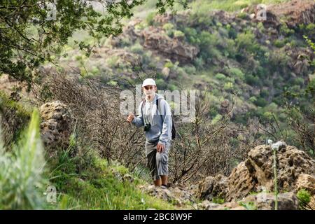 Un jeune homme dans une casquette avec un sac à dos derrière son dos voyage le long d'un itinéraire dans le parc national de Teide. Randonnée pédestre sur le sentier de montagne entouré par ende Banque D'Images