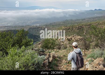 Un jeune homme dans une casquette avec un sac à dos derrière son dos voyage le long d'un itinéraire dans le parc national de Teide. Randonnée pédestre sur le sentier de montagne entouré par ende Banque D'Images