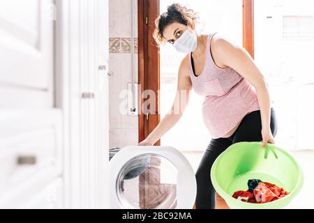 Femme enceinte portant un masque dans le visage pour empêcher les virus pendant que fait un lave-linge dans sa maison et tourne le visage vers la gauche Banque D'Images