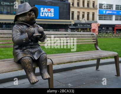 Londres. ROYAUME-UNI. 3 avril 2020. Une statue de bronze de l'ours de Paddington est assise seule sur un banc de Leicester Square, avec des messages pour le NHS sur les écrans du cinéma Odéon pendant le Global Pandemic Credit: Thomas Bowles/Alay Live News Banque D'Images