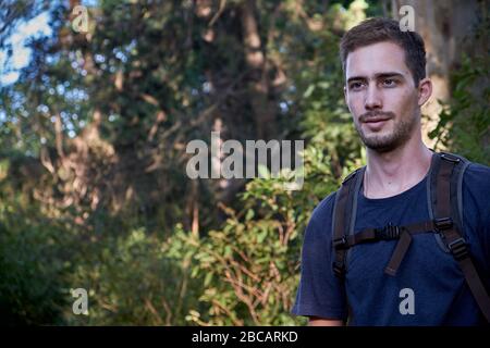 homme modèle habillé comme randonneur ou marcheur avec un sac technique sur un fond d'arbres et de branches d'une forêt Banque D'Images