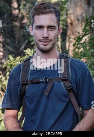 homme modèle habillé comme randonneur ou marcheur avec un sac technique sur un fond d'arbres et de branches d'une forêt Banque D'Images