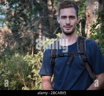 homme modèle habillé comme randonneur ou marcheur avec un sac technique sur un fond d'arbres et de branches d'une forêt Banque D'Images