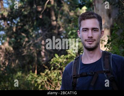 homme modèle habillé comme randonneur ou marcheur avec un sac technique sur un fond d'arbres et de branches d'une forêt Banque D'Images