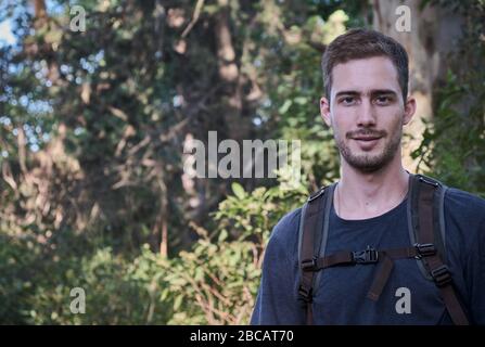 homme modèle habillé comme randonneur ou marcheur avec un sac technique sur un fond d'arbres et de branches d'une forêt Banque D'Images