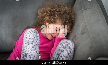 Portrait isolé et étroit d'une jeune fille de 7 ans assise dans le canapé de la pièce de départ et souriant Banque D'Images