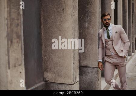Beau homme d'affaires avec lunettes de soleil se relaxant pendu sur le mur du bâtiment Banque D'Images