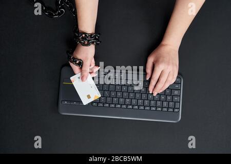 Femme avec chaîne de métal tenant la carte de crédit sur le clavier, concept de dépendance de shopping en ligne Banque D'Images