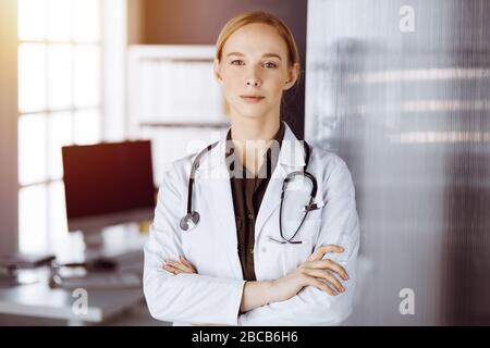 Une femme souriante et gaie se tenant debout avec les bras croisés dans la clinique. Portrait d'une femme médecin sympathique. Concept de médecine Banque D'Images