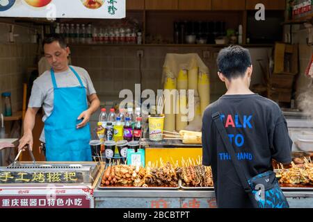 Chongqing, Chine - août 2019 : étalage de nourriture vendant de la viande frite et grillée et des collations de fruits de mer sur des bâtons de bois dans la rue Banque D'Images