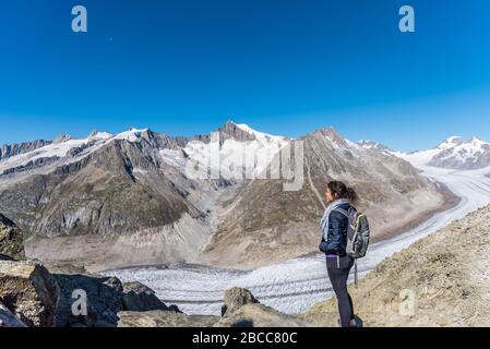 Jeune femme caucasienne avec un sac à dos sur son dos en regardant le glacier monumental d'Aletsch.ce grand ruisseau de glace, qui s'étend sur 23 km Banque D'Images