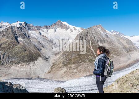 Jeune femme caucasienne avec un sac à dos sur son dos en regardant le glacier monumental d'Aletsch.ce grand ruisseau de glace, qui s'étend sur 23 km Banque D'Images