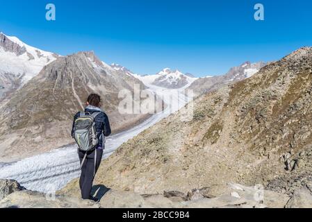 Jeune femme caucasienne avec un sac à dos sur son dos en regardant le glacier monumental d'Aletsch.ce grand ruisseau de glace, qui s'étend sur 23 km Banque D'Images