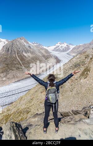 Vue de derrière une femme avec ses bras élevés regardant le glacier d'Aletsch du point de vue d'Eggishorn, Alpes bernoises, Valais du canton, Suisse, Europe Banque D'Images