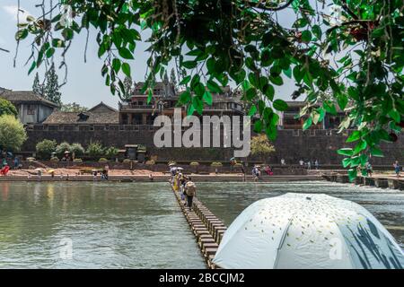 Feng Huang, Chine - Août 2019 : Femme avec parapluie traversant l'eau sur des pierres sur la rivière Tuojiang, qui traverse le centre de Fenghuang OL Banque D'Images