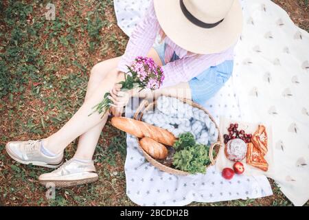 belle fille détendue dans un chapeau de paille dans la nature pique-nique panier de fleurs dans les rayons du doux coucher de soleil, camping pique-nique. Banque D'Images