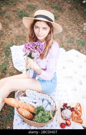 belle fille détendue dans un chapeau de paille dans la nature pique-nique panier de fleurs dans les rayons du doux coucher de soleil, camping pique-nique. Banque D'Images