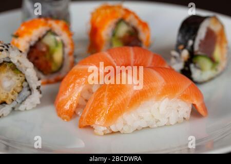 Menu à sushi avec des petits pains au saumon, au riz et au thon sur une assiette au fond noir. Cuisine japonaise. Gros plan avec mise au point sélective. Banque D'Images
