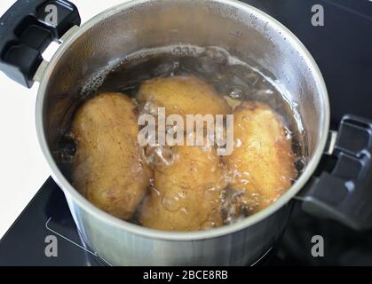 Vue de dessus des pommes de terre entières bouillonnant dans de l'eau chaude dans une casserole argentée. Banque D'Images