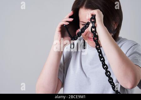 Femme parlant sur un téléphone mobile enchaîné sur fond gris, concept de dépendance Banque D'Images