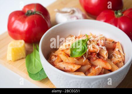 Pâtes italiennes classiques arabiata avec ses ingrédients en arrière-plan: Tomates fraîches, basilic, ail et parmesan Banque D'Images