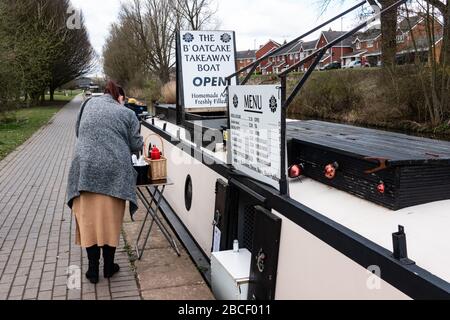 Une femme qui achète de la nourriture (gâteaux Staffordshire athakes) à partir d'un bateau à narrowboat ()que Sara, le bateau à gâteaux B'atoatcake) sur un canal, Stoke-on-Trent, Staffordshire, Royaume-Uni Banque D'Images