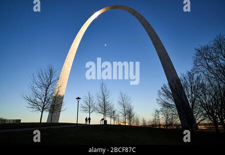 St Louis Missouri, États-Unis – 6 mars 2020 : l'arche de la porte d'entrée ; les visiteurs marchant le long de la ou des voies de la porte d'entrée au coucher du soleil tout en regardant la lune passer sous Banque D'Images