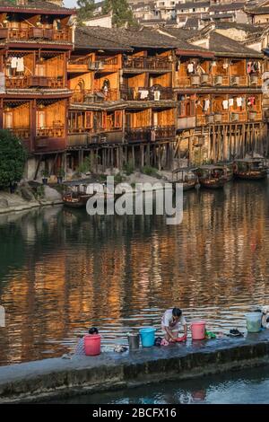 Feng Huang, Chine - Août 2019 : femmes faisant la lessive sur la rive devant les vieilles maisons historiques en bois stilt sur les rives de la rivière Tuo, f Banque D'Images