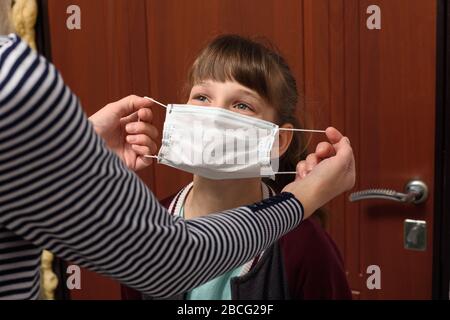 Maman met sur un enfant un masque de protection médicale avant de quitter la maison Banque D'Images