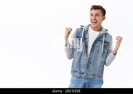 Portrait d'un homme blond joyeux et joyeux dans une veste denim, une pompe à poing atteint le but, regardant l'écran de télévision au pub comme regarder un jeu de sport Banque D'Images