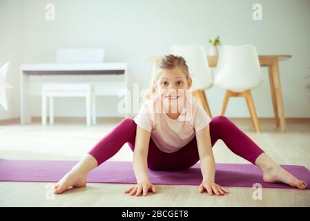 Jolie fille d'enfant heureux ayant plaisir à faire des exercices de yoga à la maison pendant la quarantaine de coronavirus Banque D'Images