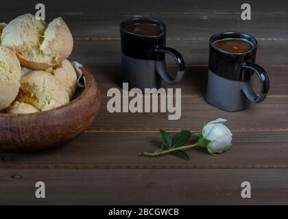 Gros plan sur le pain au fromage brésilien (Pao de queijo) sur un bol en bois, servi avec du café et du lait pour deux, sur fond de bois et de décorat Banque D'Images