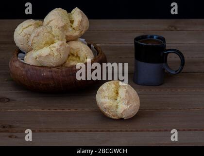 Gros plan sur le pain au fromage brésilien appétissant (Pao de quijo) sur un bol en bois, servi avec du café et du lait pour un sur fond de bois, vue de Banque D'Images