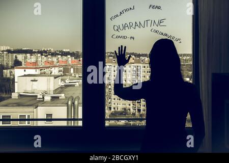 La femme en quarantaine à domicile à cause du coronavirus. Se tenir près de la fenêtre et regarder désespérément dehors. Banque D'Images