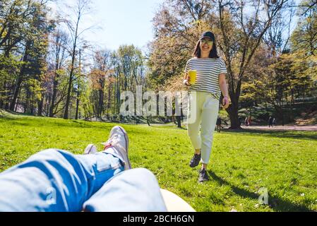 homme posé sur un canapé-lit dans un parc public femme allant et tenant une tasse de papier avec thé Banque D'Images