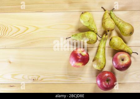 Plusieurs poires mûres juteuses de la variété de conférence anglaise et trois pommes rouges se trouvent sur une table en bois texturé. Espace pour le texte Banque D'Images