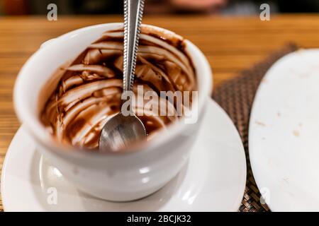 Gros plan de la cuillère sale à l'intérieur de la tasse de chocolat fondu chaud dans une petite théière blanche sur la plaque de soucoupe mangée avec personne Banque D'Images