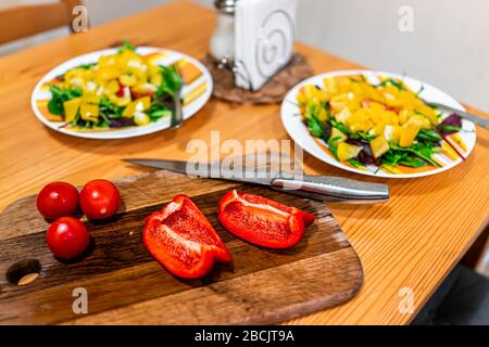 Hacher des légumes frais sur la table de découpe avec deux assiettes de salade végétalienne avec des poivrons jaunes rouges et des tomates Banque D'Images