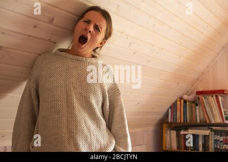 Jeune femme souriante se bâillant debout près du mur de bois étant seule en quarantaine. Banque D'Images