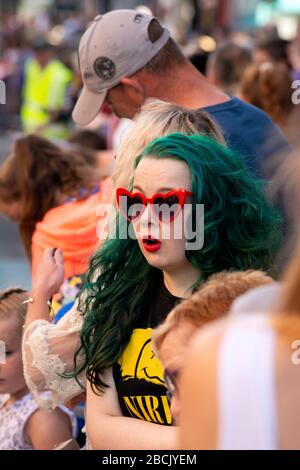 Jeune femme flamboyante avec des cheveux de couleur verte et des lunettes rouges faisant une drôle d'expression faciale assistant à la parade de rue Banque D'Images