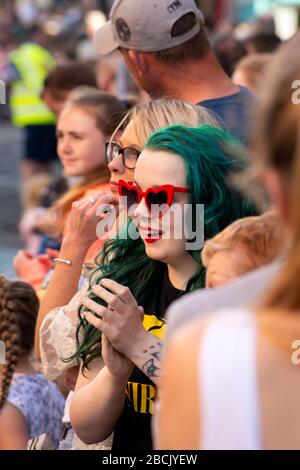 Jeune femme flamboyante aux cheveux de couleur verte faisant des expressions drôles du visage parmi la foule de personnes assistant aux célébrations de rue pour le 4th juillet Parade et les célébrations du jour de l'indépendance à Killarney, en Irlande Banque D'Images