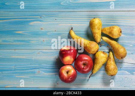 Plusieurs poires mûres juteuses de la variété de conférence anglaise et trois pommes rouges se trouvent sur une table en bois bleu texturé. Espace pour le texte Banque D'Images