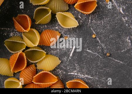 Pâtes Conchiglie Rigate, mélange de coquillages colorés non cuits dispersés sur la table, a laissé un espace vide. Cuisine italienne texturée concept de fond. Haut Banque D'Images