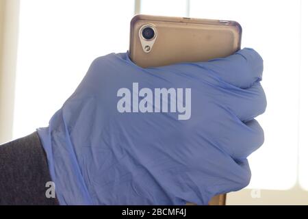 Un homme en gants bleus tient un téléphone portable, des mesures de protection et de prudence contre le virus corona Banque D'Images